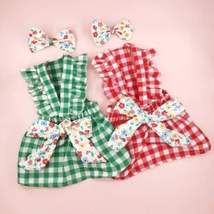 Plaid Christmas dog dresses in red and green with floral bow accessories, flat lay view