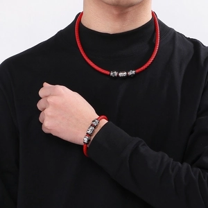 Close-up of woven red leather cord necklace and bracelet with metallic skull beads