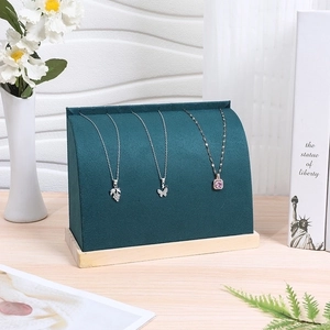 Detail of dark green velvet necklace display stand with natural wooden base in soft light