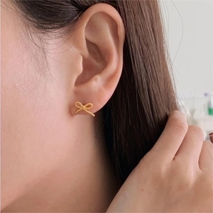 Close-up of golden bow-shaped stud earrings with twisted metal texture on a model