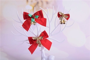 Three red velvet Christmas bows with holly leaves and gold bells on a white display stand