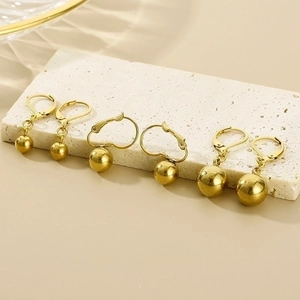 Detailed close-up of golden spherical drop earrings displayed on a textured stone stand