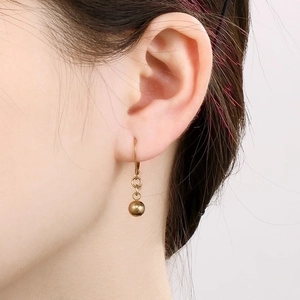 Detailed close-up of polished gold bead drop earrings on model with high gloss finish