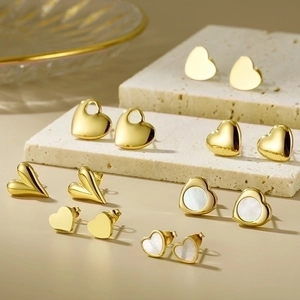 Collection of gold heart stud earrings with glossy finish on textured stone base