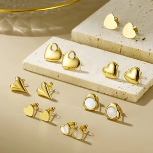 Detailed close-up of 18K gold plated heart stud earrings on beige stone display
