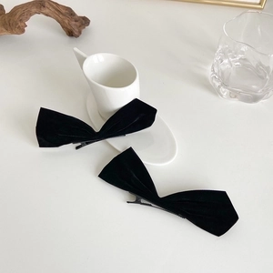 Detail of two black velvet bow hair clips with metal duckbill clips on a clean white table