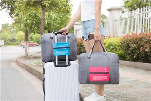 Detail view of the foldable travel bag attached to a suitcase handle with front pocket