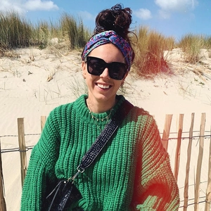 Frau im grünen Grobstrickpullover und schwarzer quadratischer Sonnenbrille am Sonnenstrand