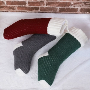 Close-up of trio knitted Christmas stockings in burgundy, grey and green on plush surface