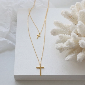 Dettaglio di una collana a doppio strato con croce d'oro su supporto bianco minimale