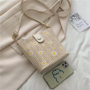 Detail of straw bucket bag with daisy prints and gold buckle on beige fabric background