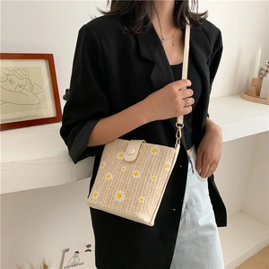Detail view of straw bucket bag with daisy prints and leather strap on model