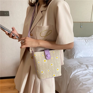 Straw bucket bag with purple PU strap and daisy print shown on shoulder