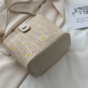 Chic woven bucket bag with daisy prints and leather base on soft fabric background