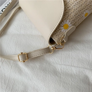 Close-up of straw woven bucket bag with white daisy print and adjustable PU leather strap
