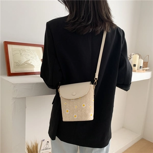 Detail of straw woven bucket bag featuring daisy floral patterns and adjustable PU strap