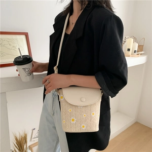 Detail of straw woven bucket bag featuring daisy pattern and cream PU leather strap