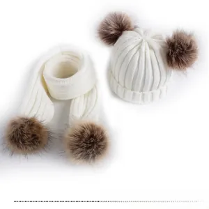 Macro shot of white knitted baby hat and scarf set with brown faux fur pom-poms