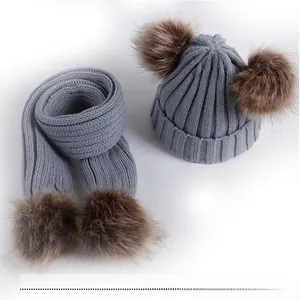 Flat lay of gray knit baby hat and scarf set with brown faux fur pom poms for winter
