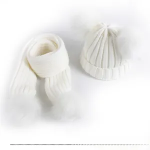 Detailed view of white knit baby hat and scarf set with soft faux fur double pom-poms