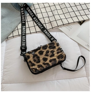 Close-up of leopard print mini suitcase crossbody bag with Forever Young strap on a bed