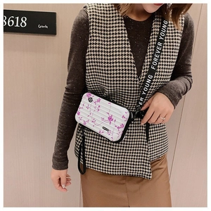 Close-up of a mini white suitcase crossbody bag with purple floral patterns on model