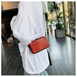 Detail of red mini hardshell suitcase crossbody bag with textured grooves and printed strap
