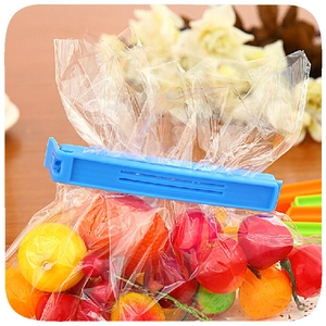 Blue plastic food bag sealer clip shown sealing a fruit bag on a bright tabletop