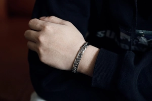 Close-up of a silver curb chain bracelet with a square clasp worn on a male wrist