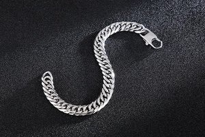 Macro shot of silver curb chain bracelet with lobster clasp on a black textured surface