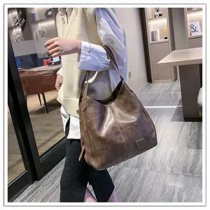 Detailed side view of a large brown leather tote bag worn by a model in a modern room