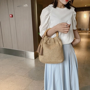 Fashionable light brown straw handbag with wooden handles and tassels on a model