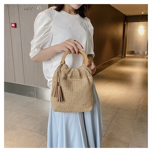 Detail of hand-woven straw bag with round wooden handle and stylish tassel charm