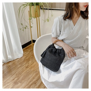 Close-up of black woven straw bucket bag with round wooden handles and tassel detail