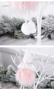 Detail of plush pink Christmas angel ornament with white wings hanging on snowy branches