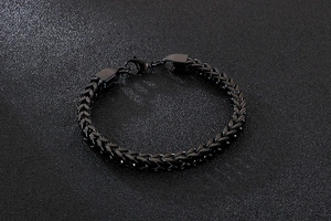 Close-up of black braided stainless steel chain bracelet with metallic luster on textured surface