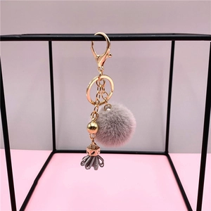 Gray faux fur pompom keychain with gold hardware and leather tassel on geometric frame