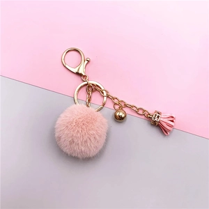 Detail of pink faux fur pompom keychain with golden metal clasp and leather tassel