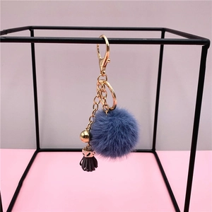 Detail of blue faux fur pompom keychain with grey tassel and gold metal hardware