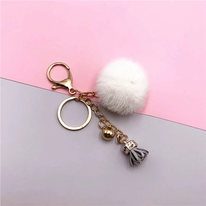Detail of white faux fur pompom keychain with grey tassel and gold metal hardware