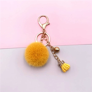 Detailed shot of yellow plush pompom keychain with golden bell and leather tassel detail