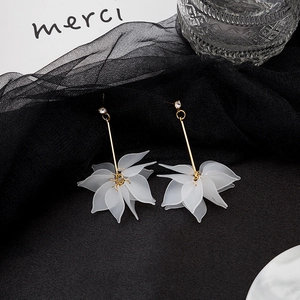 Detail of long drop earrings featuring white petals and delicate gold rods on black mesh