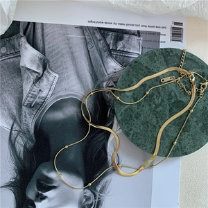 Detail of a gold double-layer necklace featuring a flat snake chain and small metal beads