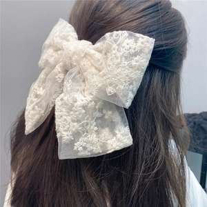Detail showing the white lace bow hair clip with floral embroidery on brown hair