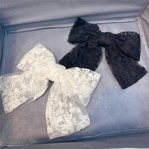 Detail of layered lace bow hair clips in black and cream featuring floral embroidery patterns