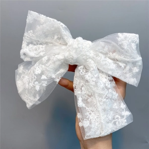 Close-up of a large white lace bow hair clip with floral embroidery held by hand
