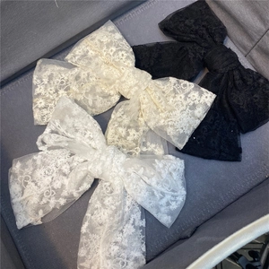 Detailed close-up of large layered lace bow hair clips in black, beige, and white colors