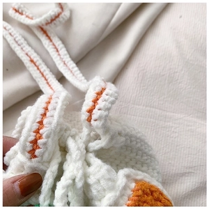 Close-up of handmade white knit bucket bag with orange drawstring details and woven texture