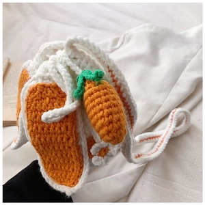 Detail of handmade crochet carrot bucket bag with orange yarn and green leaf decor