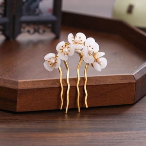 Detailed close-up of a U-shaped hair pin with white flowers and pearls on a wooden tray